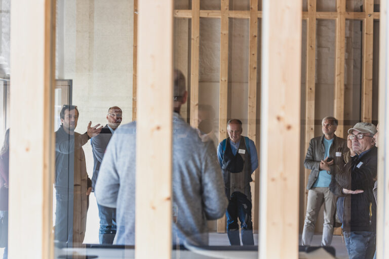 Menschen stehen bei einer Führung in einem Gebäude aus Holz.